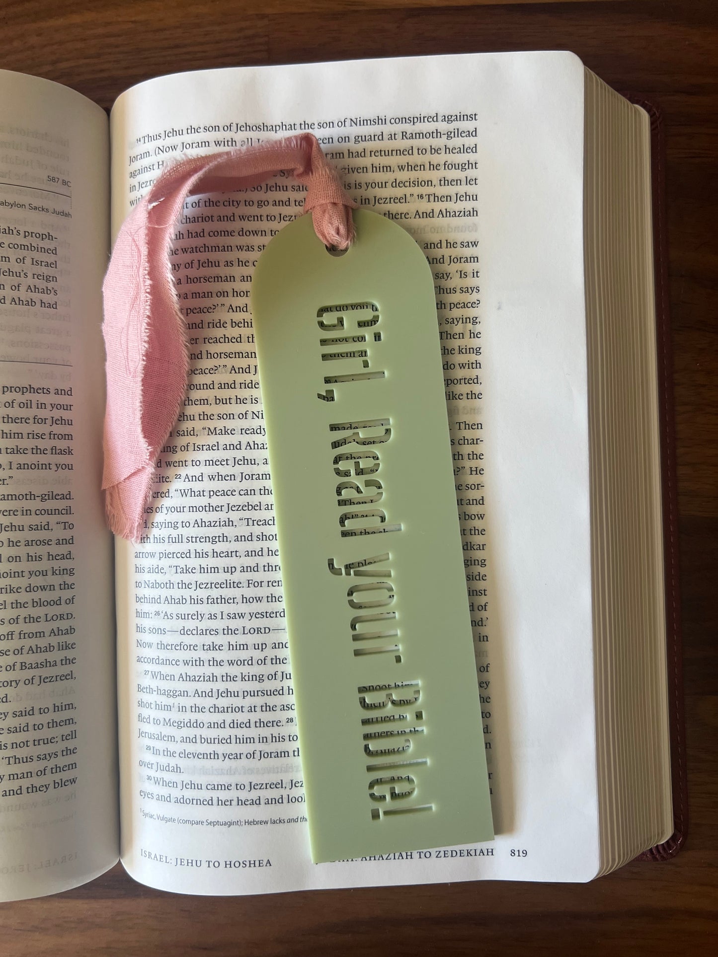 Girl reading her Bible bookmark from Sons & Daughters featuring inspirational message and colorful design.