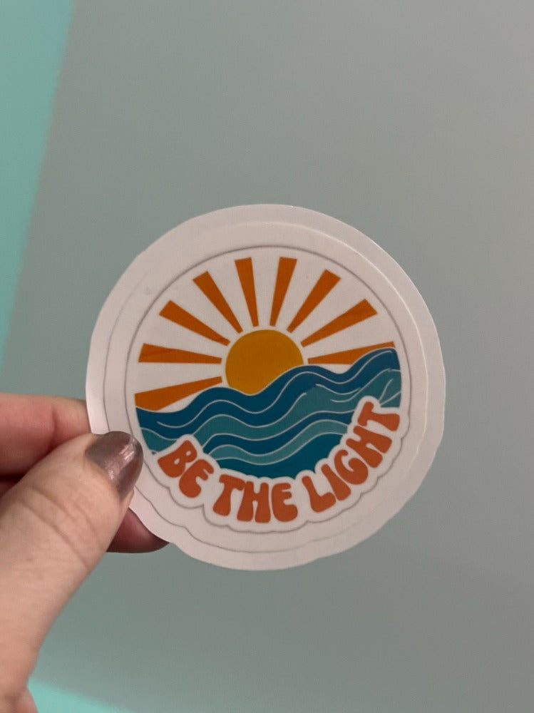 Decorative wall art featuring the phrase "Be The Light" in stylish lettering, perfect for inspiring home or office decor.