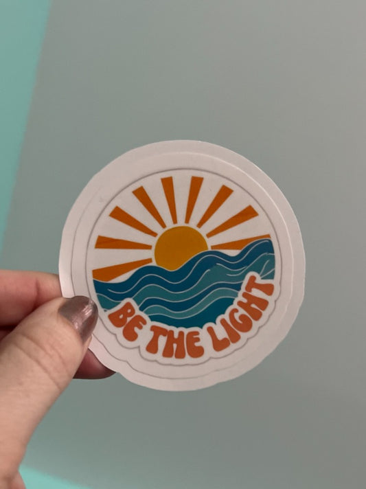 Decorative wall art featuring the phrase "Be The Light" in stylish lettering, perfect for inspiring home or office decor.