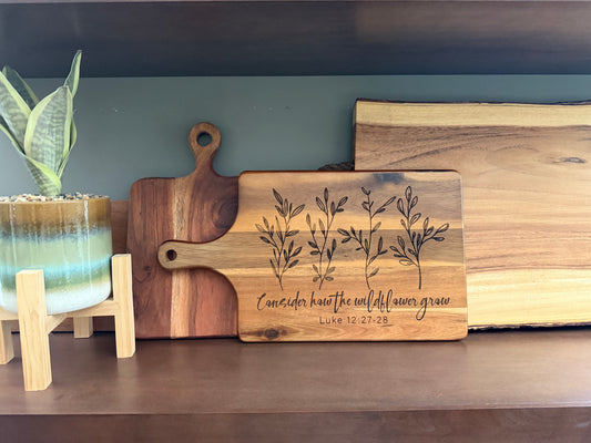 Faith inspired engraved acacia wood cutting board with scripture Luke 12:27-28, Christian kitchen decor, rustic farmhouse style.