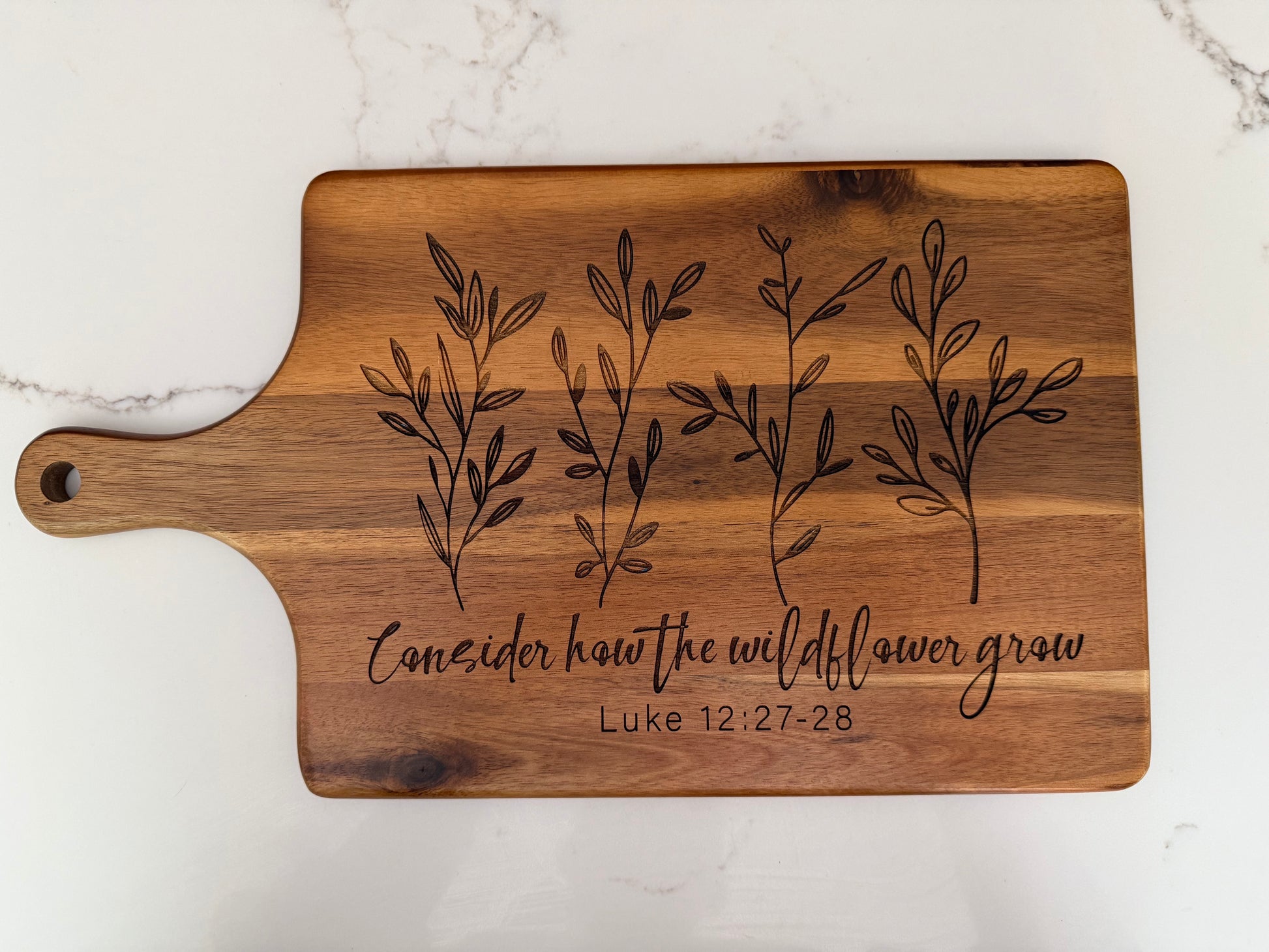 Faith inspired engraved acacia wood cutting board with scripture Luke 12:27-28, Christian kitchen decor and rustic farmhouse display.