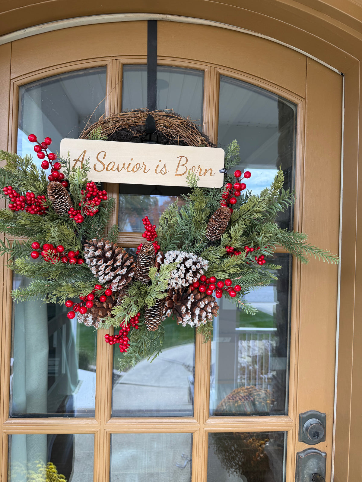 A Savior Is Born door wreath by Sons & Daughters with festive Christian lettering and seasonal greenery