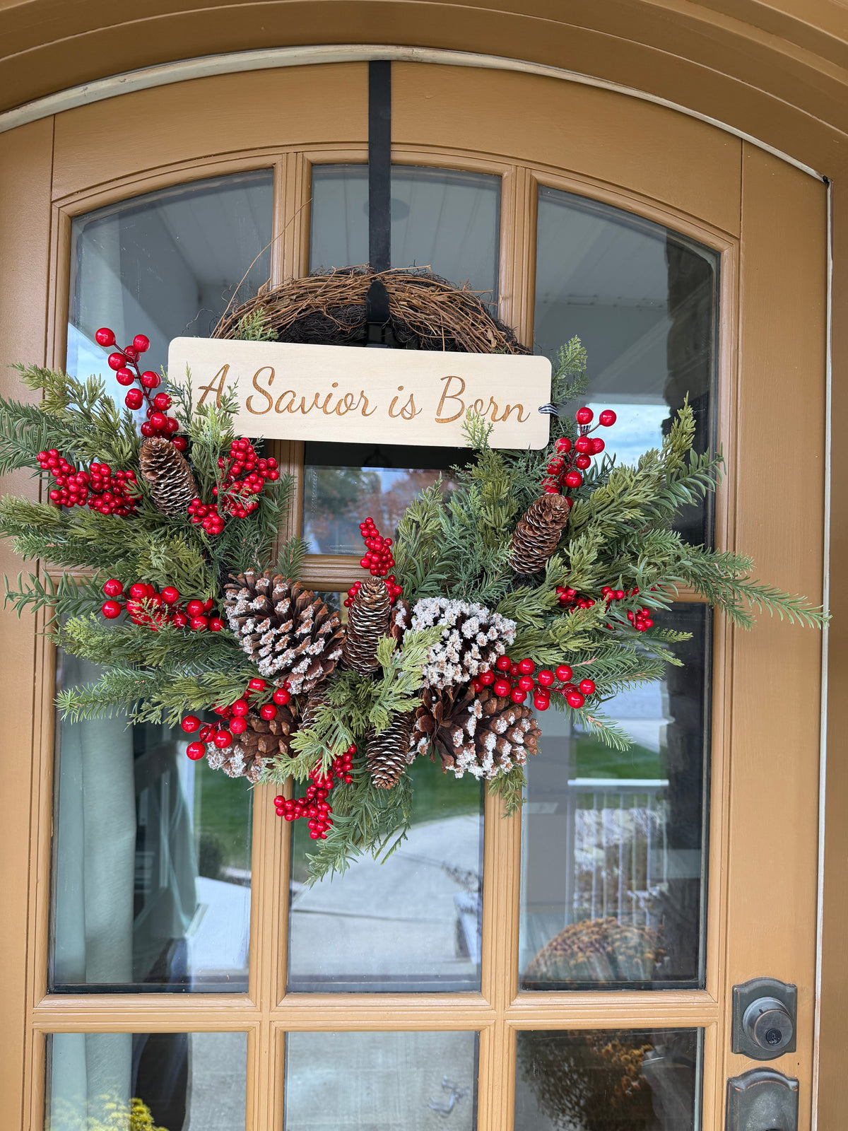 Sons & Daughters “A Savior Is Born” door wreath with festive lettering and holiday greenery